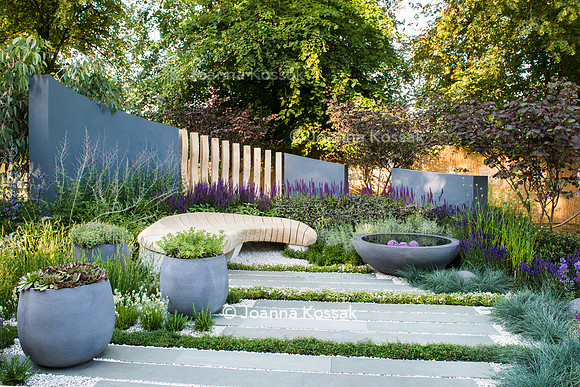 H U G: Healing Urban Garden; view of a modern patio with wooden bench and circular concrete water feature and containers amongst  Festuca glauca (blue fescue grass), Thymes, Lavandula, Nepeta. - Desig