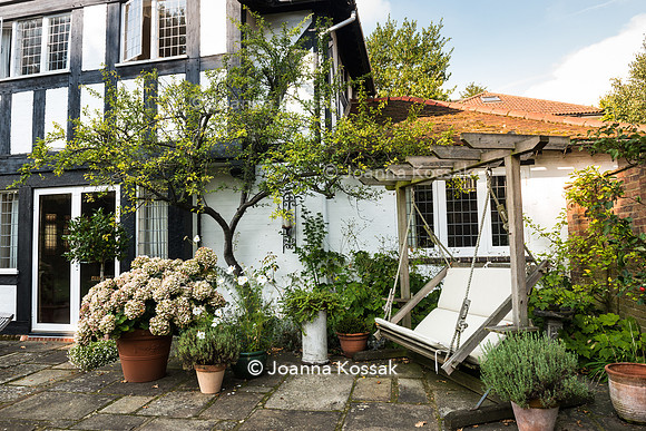 Garden swing seat and mix of summer plants in flowerpots on the patio