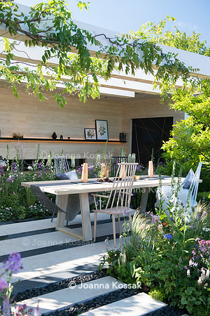 Patio with wooden chairs and table (by Nils Verweij), the path made from limestone paving slabs and separated with black oval stones surrounded by Stipa tenuissima, Tiarella 'Spring symphony', Digital