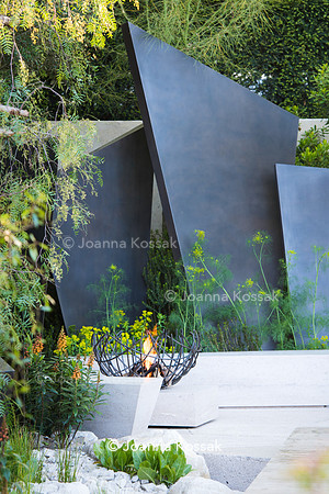 Seating area with  stone benches and metal fire bowl burner in front of irregular geometric bronze sculptures (fins)
