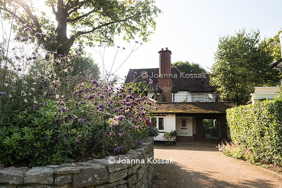 Flowerbed surrounded by stone border wall planted with Verbena bonariensis, Gaura lindheimeri and Sedum in front of the house.