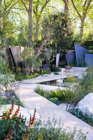 Irregular geometric bronze sculptures (fins), seating area with stone benches, limestone paths surrounded by stones, Isoplexus (Isoplexis) canariensis - Canary Island Foxgloves, Maytenus boaria, Schin