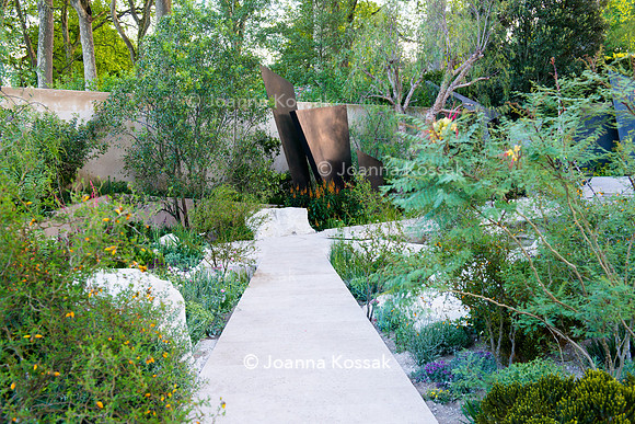 Irregular geometric bronze sculptures (fins), stones and  limestone paths surrounded by  Maytenus boaria, Schinus molle.
